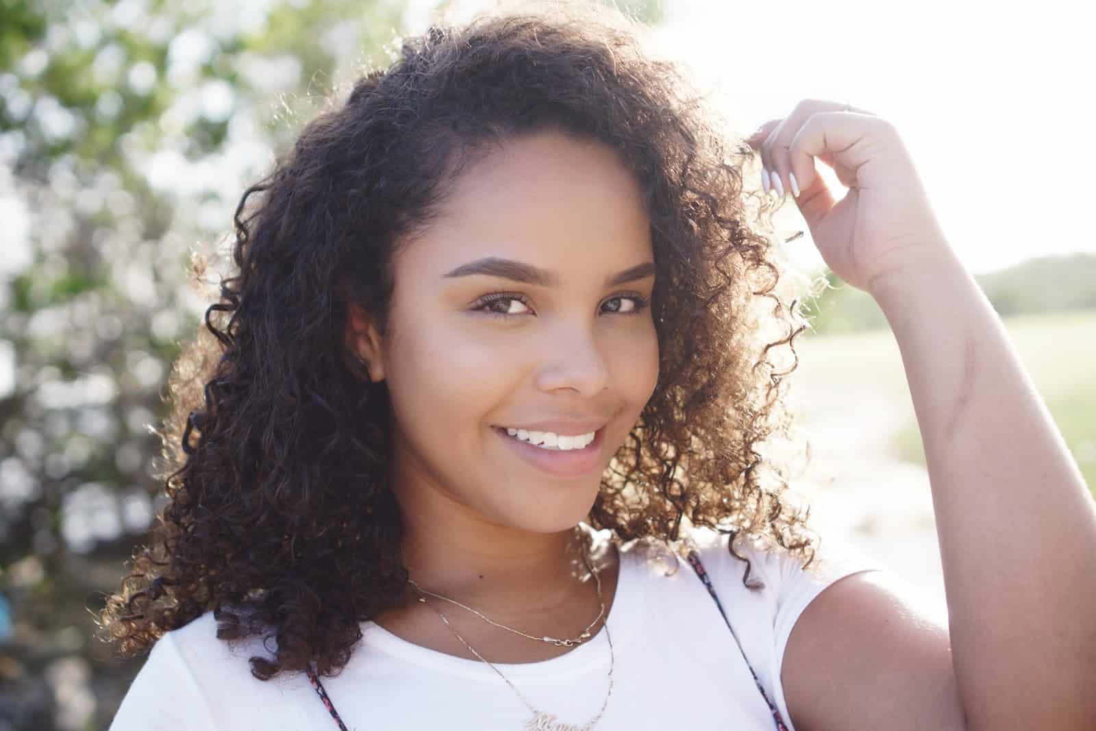 Woman in a white tee-shirt standing outdoors and smiling.