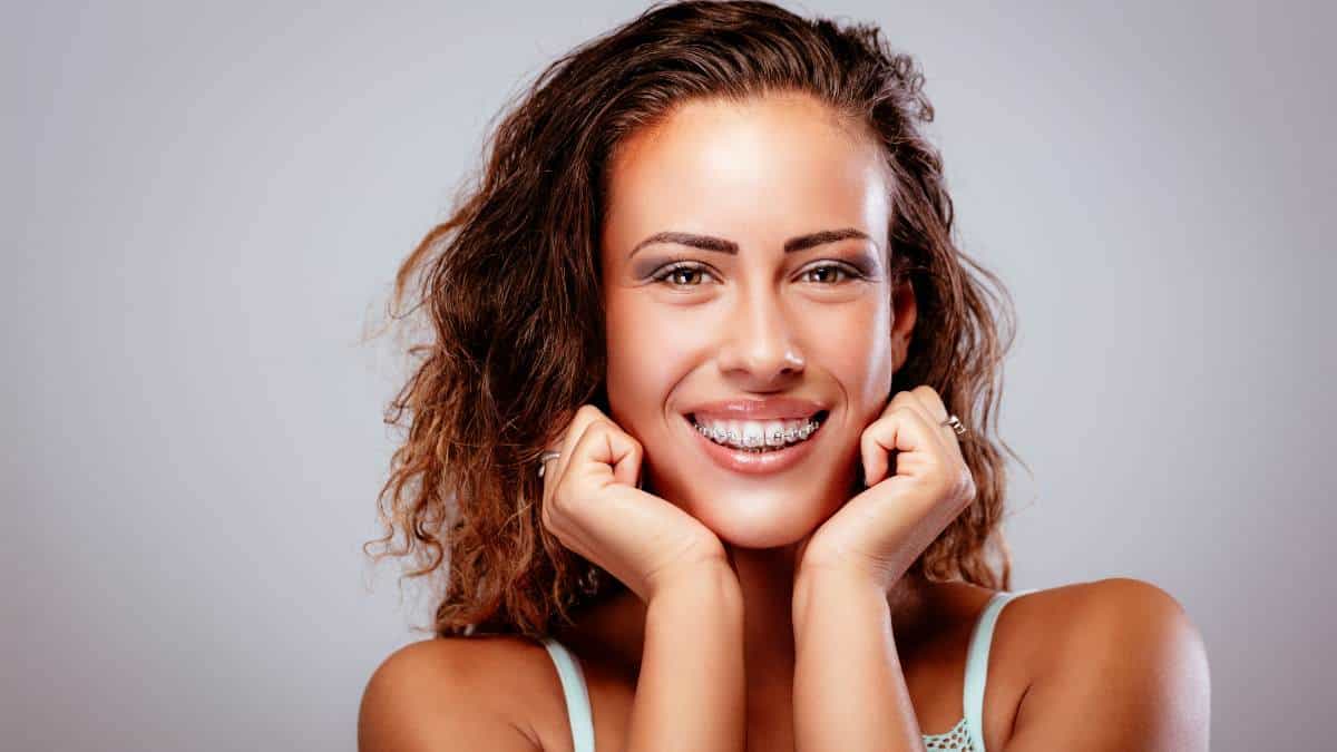 Woman with braces smiling and holding her hands to her chin.