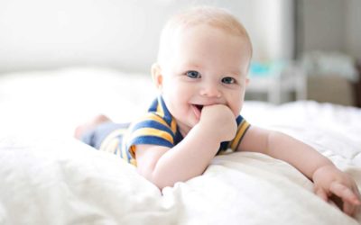 Baby lying on a bed and sucking their thumb.