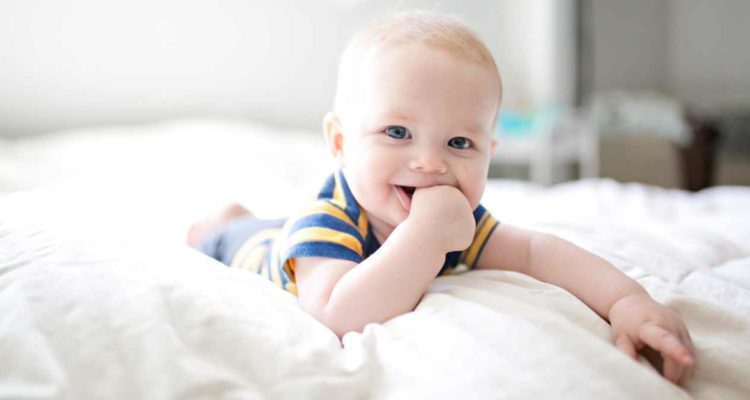 Baby lying on a bed and sucking their thumb.