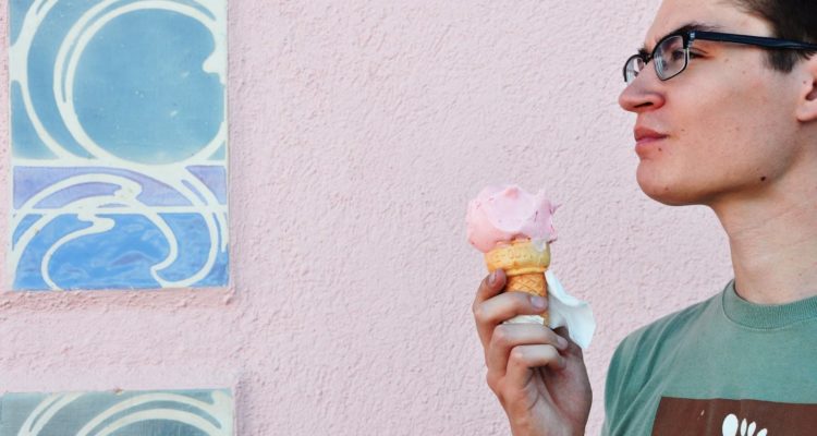 Man standing in front of a pale pink wall holding an ice cream cone.