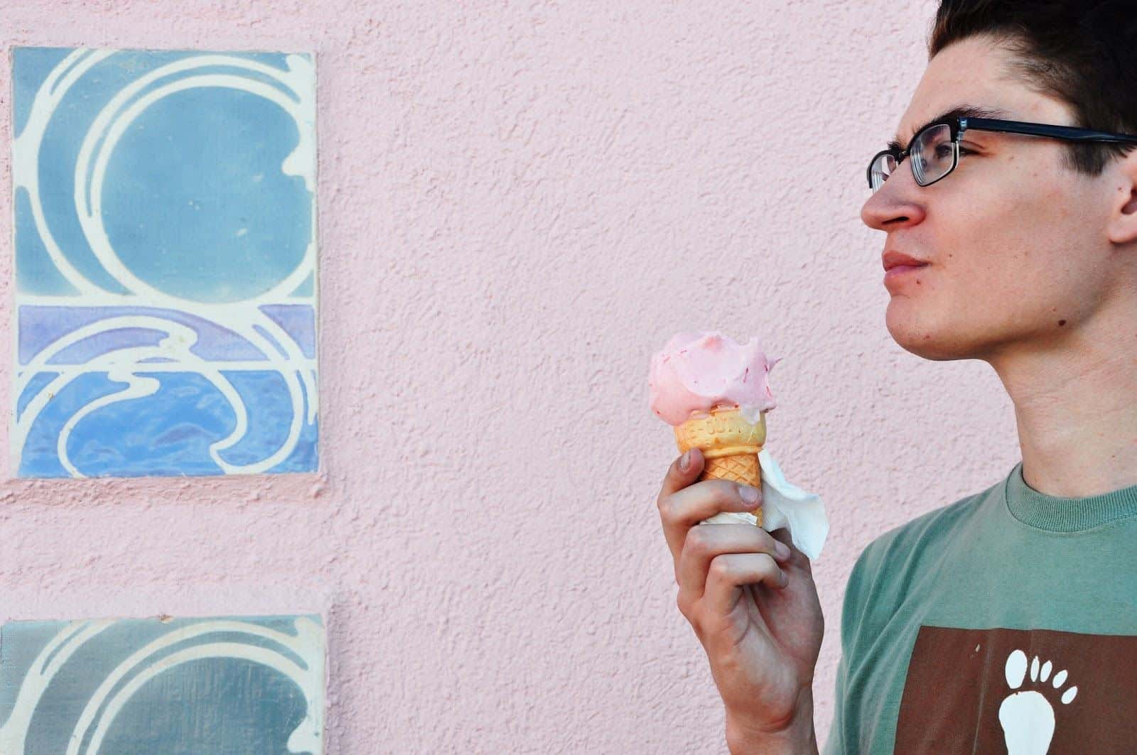 Man standing in front of a pale pink wall holding an ice cream cone.