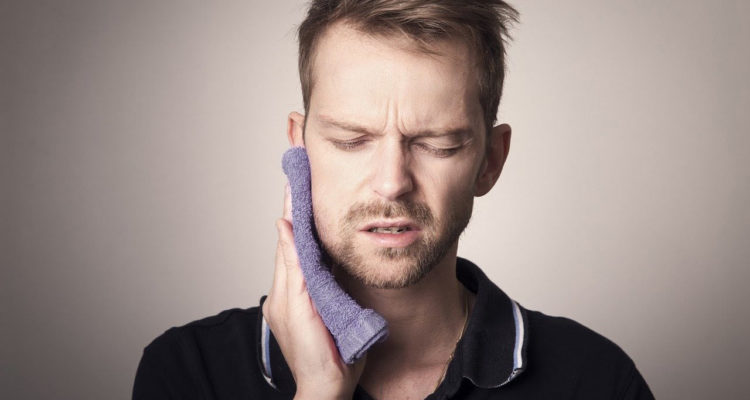 Man pressing a cloth to his jaw and looking pained.