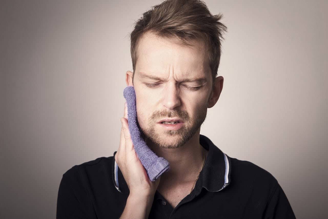 Man pressing a cloth to his jaw and looking pained.