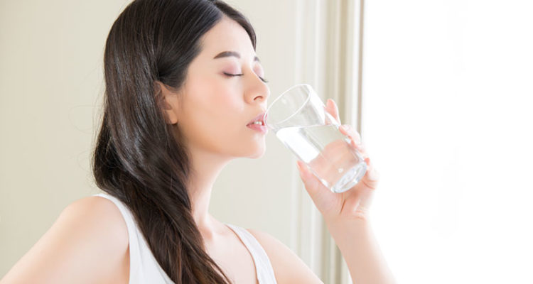 Woman in a white tank top drinking a glass of water.