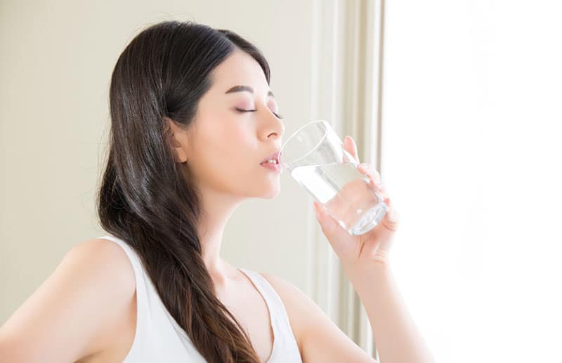 Woman in a white tank top drinking a glass of water.