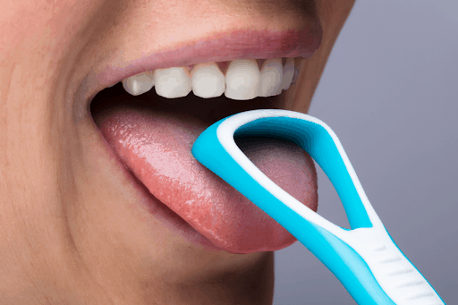 A person using a plastic scraper to clean their tongue.