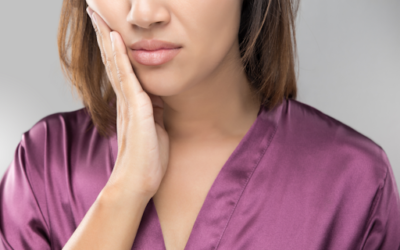 Woman in a purple shirt holding her jaw in pain.