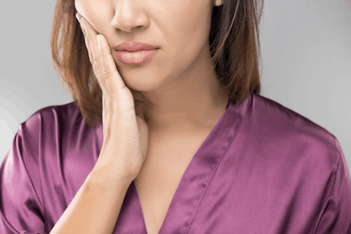 Woman in a purple shirt holding her jaw in pain.